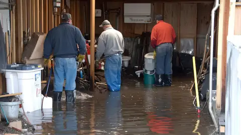 Three workers in boots standing in water inside a flooded basement
